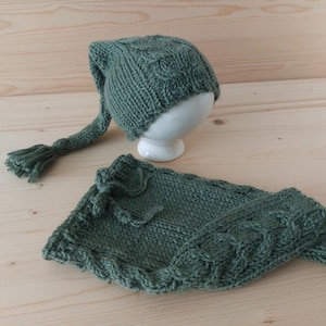 May include: A green knitted hat with a long tail and a matching green knitted mitten. The hat and mitten are made with a cable knit pattern.