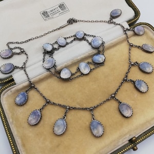 May include: A silver necklace and bracelet set featuring blue and white cameo stones. The necklace has a drop design with multiple stones hanging from the chain. The bracelet is a simple chain with multiple stones.