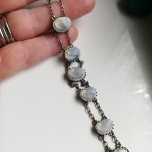 May include: A silver chain bracelet featuring seven oval moonstone gemstones. The stones are set in silver bezels and linked by a fine silver chain.