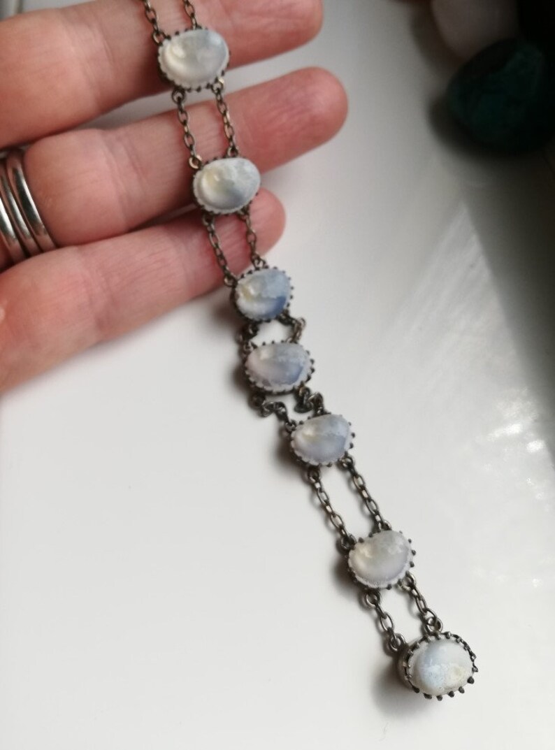 May include: A silver chain bracelet featuring seven oval moonstone gemstones. The stones are set in silver bezels and linked by a fine silver chain.