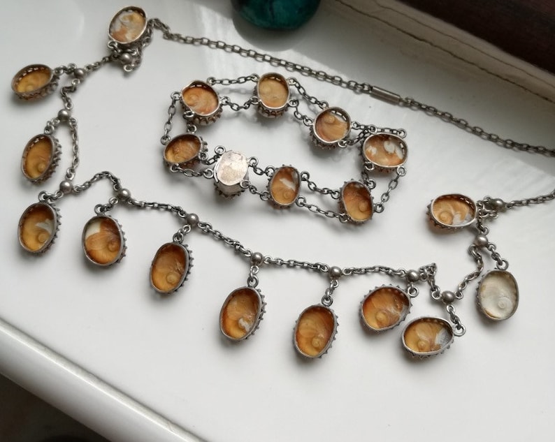 May include: A silver chain necklace with multiple oval-shaped amber stones. The necklace has a long, dangling chain with several smaller amber stones.