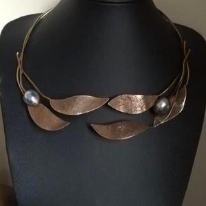 May include: A unique necklace featuring a silver-toned wire design with bronze-colored leaf-shaped pendants. Two dark gray, spherical beads are incorporated into the design, adding a touch of elegance to this handcrafted jewelry piece.