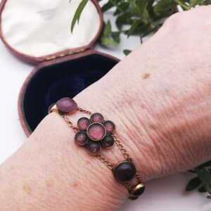 May include: A vintage gold bracelet with a floral design. The bracelet features a central flower with pink and purple stones, connected by delicate chain links. Additional oval-shaped stones are set along the chain.