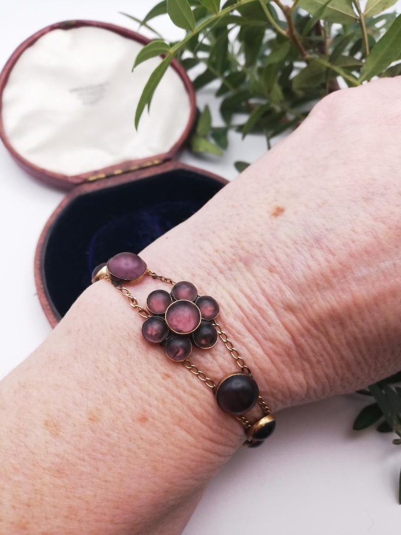 May include: A vintage gold bracelet with a floral design. The bracelet features a central flower with pink and purple stones, connected by delicate chain links. Additional oval-shaped stones are set along the chain.