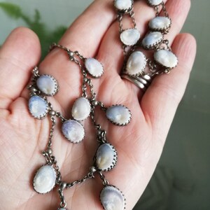 May include: A silver chain necklace with a pendant made of multiple oval-shaped white and blue iridescent shells. The shells are set in silver frames.