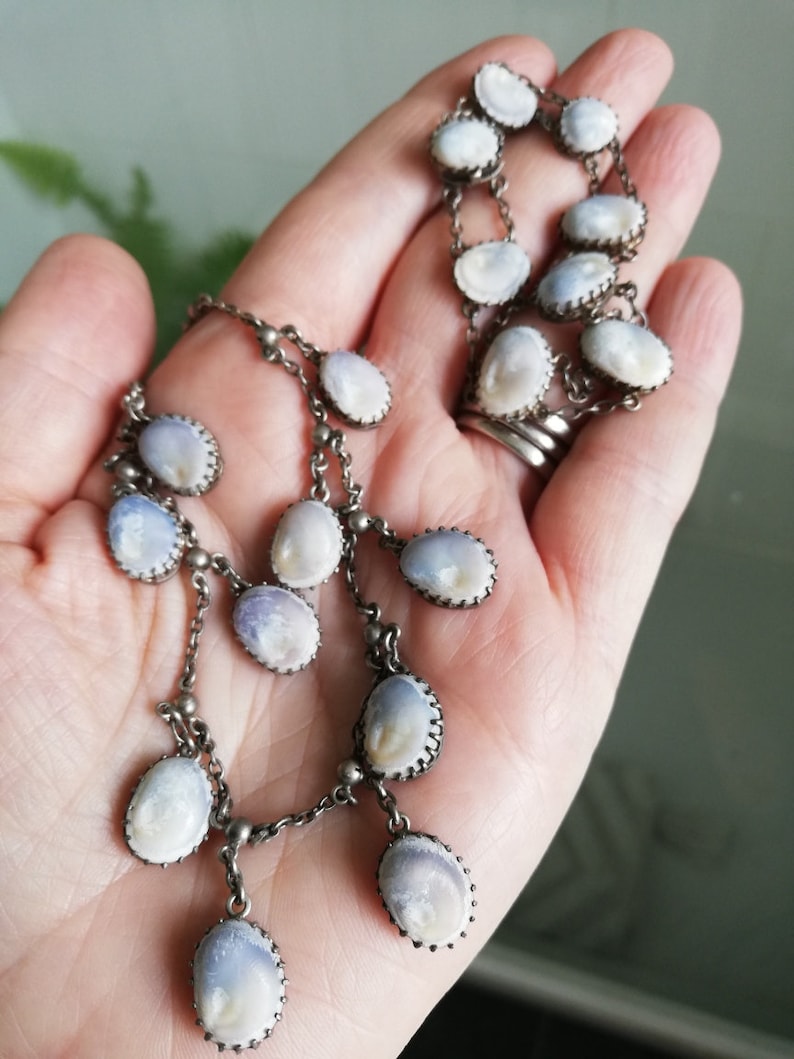 May include: A silver chain necklace with a pendant made of multiple oval-shaped white and blue iridescent shells. The shells are set in silver frames.