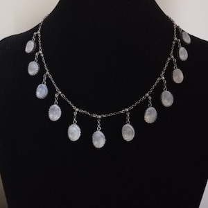May include: A silver chain necklace with multiple oval-shaped moonstone pendants. The necklace is on a black background.
