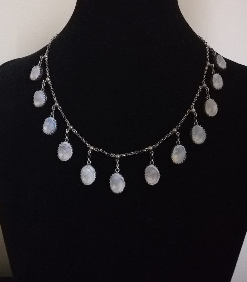 May include: A silver chain necklace with multiple oval-shaped moonstone pendants. The necklace is on a black background.