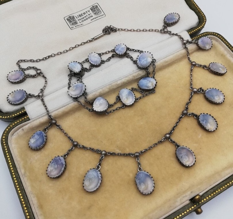 May include: A silver necklace and bracelet set featuring blue and white cameo stones. The necklace has a drop design with multiple stones hanging from the chain. The bracelet is a simple chain with multiple stones.