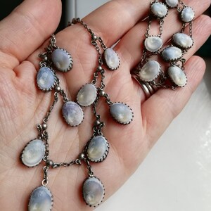 May include: A silver chain necklace with multiple strands and oval-shaped pendants. The pendants are made of a white, iridescent material with a silver trim.