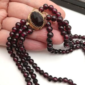 May include: A vintage garnet necklace with multiple strands of deep red beads. The necklace features a central gold-toned oval pendant with a faceted garnet stone. The beads are small and round, creating a classic and elegant jewelry piece.