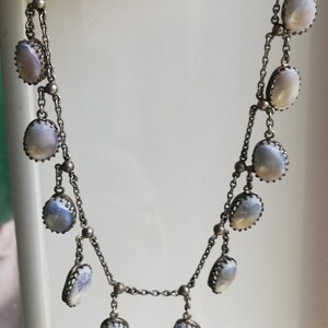 May include: A silver chain necklace with multiple oval-shaped, iridescent blue stones. The stones are set in silver and have a delicate, ornate design.