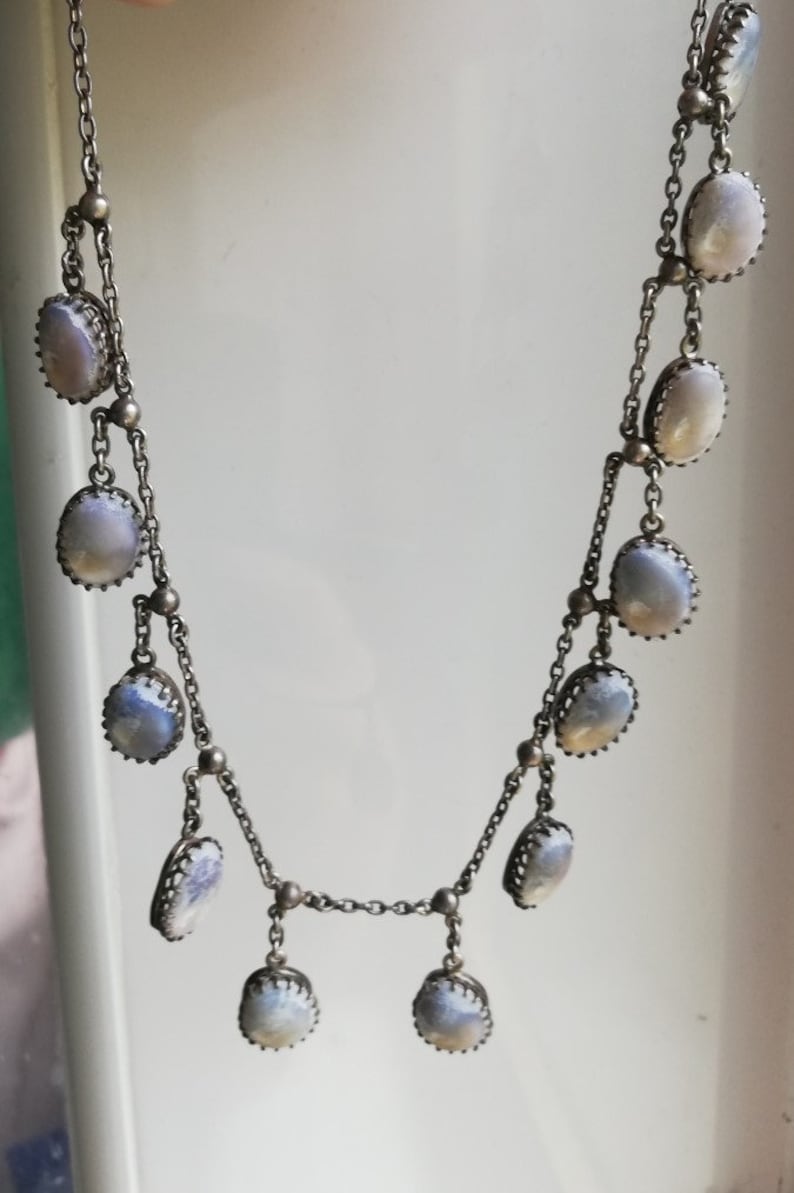 May include: A silver chain necklace with multiple oval-shaped, iridescent blue stones. The stones are set in silver and have a delicate, ornate design.