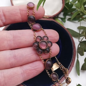 May include: A vintage gold bracelet with mauve-coloured oval and circular stones, arranged in a floral pattern. The bracelet is displayed in a vintage jewellery box with a blue interior and a pink exterior.