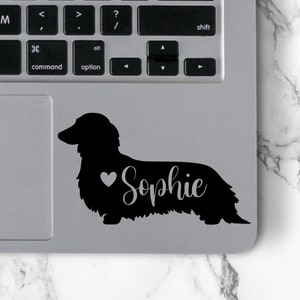 May include: Black silhouette of a dachshund with a heart and the name "Sophie" on a silver laptop.