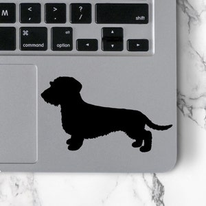 May include: A black silhouette of a dachshund dog on a silver laptop.