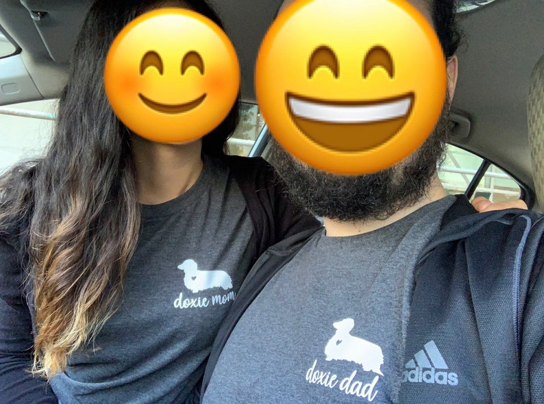 May include: A couple wearing matching gray t-shirts with a dachshund silhouette and the text "doxie mom" and "doxie dad". The man is wearing a black Adidas jacket.