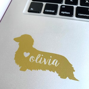 May include: Gold dachshund silhouette sticker with a white heart and the name "olivia" written in cursive.