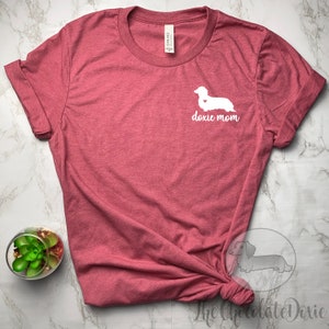May include: A maroon t-shirt with a white dachshund silhouette and the text "doxie mom" on the front.