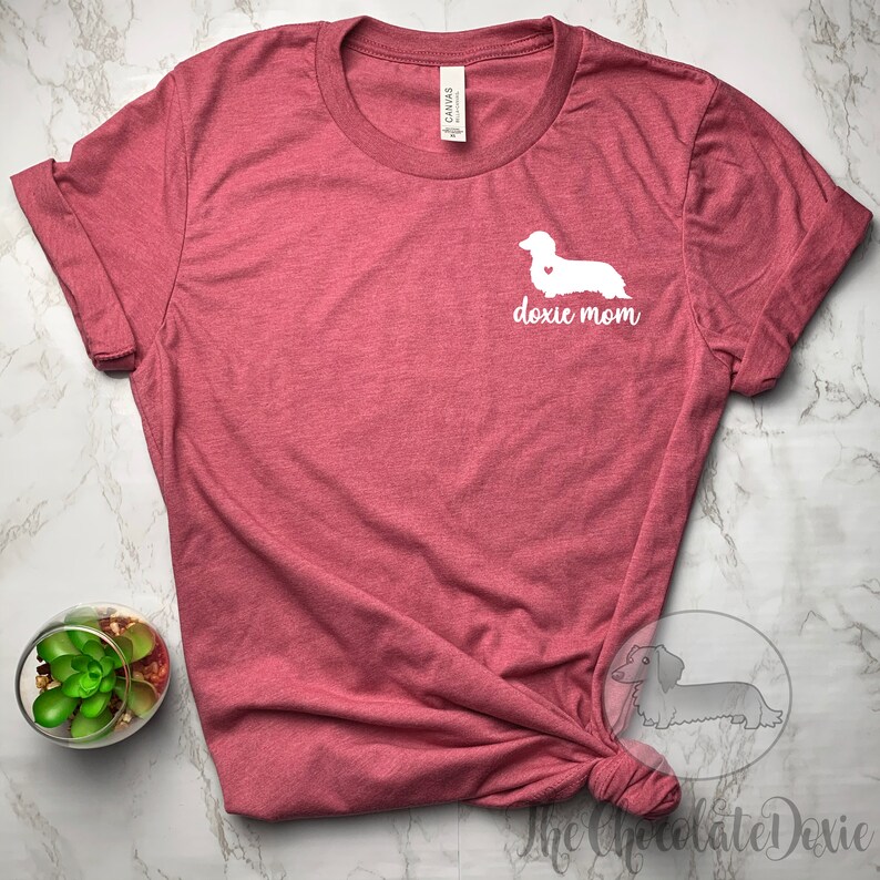 May include: A maroon t-shirt with a white dachshund silhouette and the text "doxie mom" on the front.