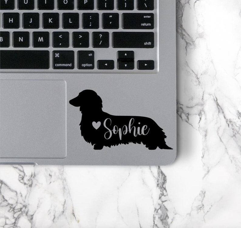 May include: Black silhouette of a dachshund with a heart and the name "Sophie" on a silver laptop.
