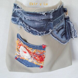 May include: A beige fabric bag with denim accents. The bag features a denim flap, a denim pocket with colorful embroidery, and a denim tassel. The text "Ekir y Lu" is visible at the top.