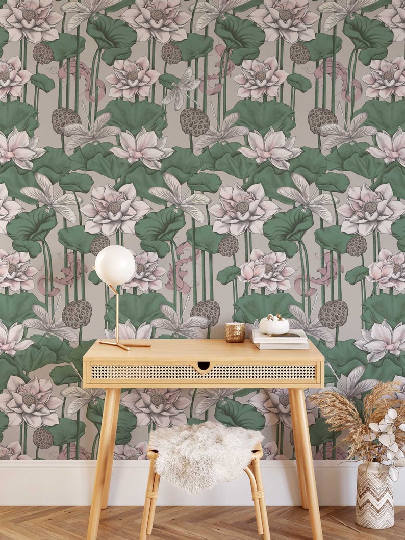 Puede incluir: Un papel tapiz floral gris claro y verde con un patr&oacute;n de flores de loto rosas. Un escritorio de madera con un caj&oacute;n de rat&aacute;n tejido se encuentra frente al papel tapiz. Un taburete blanco esponjoso y un jarr&oacute;n con hierba de pampa seca tambi&eacute;n est&aacute;n en la imagen.