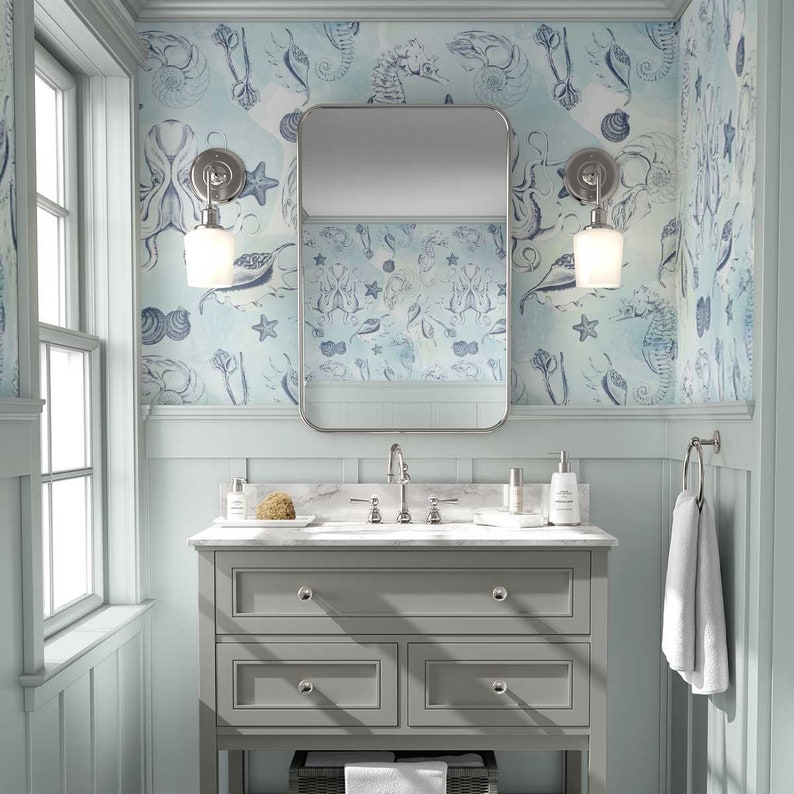 Puede incluir: Un tocador de ba&ntilde;o con un gabinete gris y una encimera blanca. El tocador tiene tres cajones y un espejo encima. Las paredes est&aacute;n cubiertas con papel tapiz azul y blanco con un tema n&aacute;utico. El papel tapiz presenta caballitos de mar, conchas y otros dise&ntilde;os inspirados en el oc&eacute;ano.