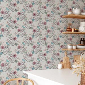 May include: A white wallpaper with a repeating pattern of a skull made of branches with pink flowers and blue birds. The wallpaper is shown in a kitchen setting with shelves and kitchen supplies.