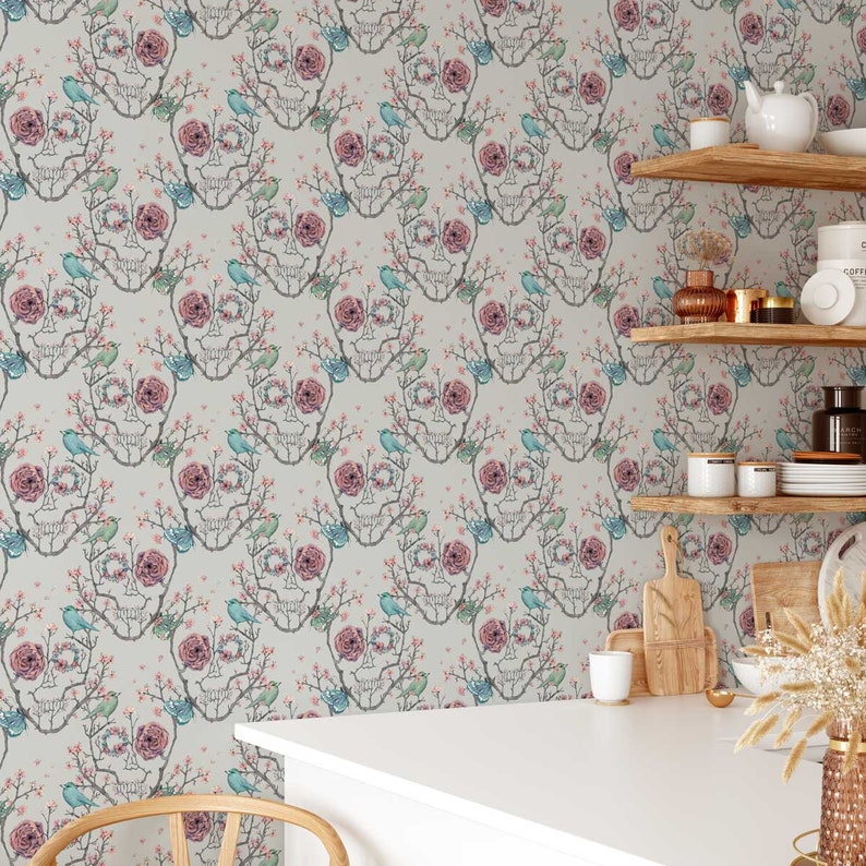 May include: A white wallpaper with a repeating pattern of a skull made of branches with pink flowers and blue birds. The wallpaper is shown in a kitchen setting with shelves and kitchen supplies.