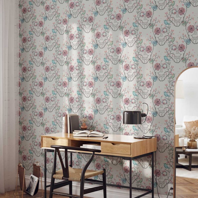 May include: A white wallpaper with a repeating pattern of pink and blue flowers and skulls. The wallpaper is in a room with a desk, chair, and lamp.
