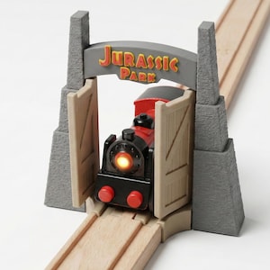 Pode incluir: Um conjunto de comboios de brinquedo com uma locomotiva vermelha e preta e um farol brilhante, passando por um arco do Jurassic Park. O arco tem o logotipo do Jurassic Park em amarelo. O comboio está em carris de madeira.