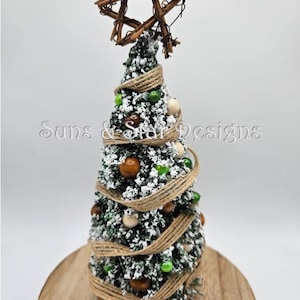 May include: A small, snowy, green artificial Christmas tree decorated with brown and white wooden beads, green glass beads, and a brown hessian ribbon. The tree is topped with a rustic twig star and sits on a wooden base.