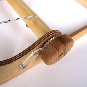K&ouml;nnte beinhalten: Ein Holzwebstuhl mit einem wei&szlig;en und schwarzen Faden, der um die obere Rolle gewickelt ist. Der Webstuhl hat einen Holzspannknauf mit einem Zahnradmechanismus.