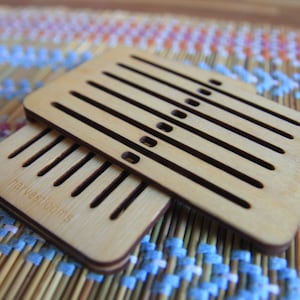 May include: Two wooden weaving looms with slots for yarn. The top loom has a label that reads "harvestlooms".
