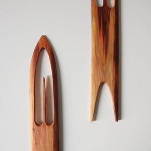 May include: Two wooden knitting needles with a pointed tip and a carved loop at the top. The needles are made of a reddish-brown wood with a natural grain pattern.