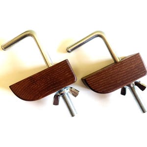 May include: Two woodworking clamps with dark brown wooden blocks, silver metal L-shaped handles, and threaded bolts with wing nuts. The clamps are designed to hold pieces of wood together during construction or repair.