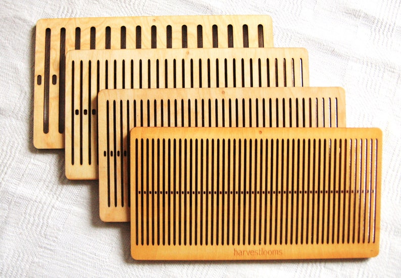 May include: Four wooden weaving looms of different sizes, stacked on top of each other. The looms are made of light brown wood with dark brown slots for weaving. The largest loom has the text "harvestlooms" printed on the bottom.