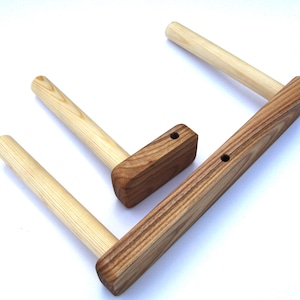 Puede incluir: Dos barras para toallas de madera con un acabado de madera natural. Las barras están montadas en una base rectangular de madera con una mancha marrón oscura. La base tiene dos agujeros para montaje.