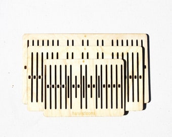 Könnte beinhalten: Satz von drei Holzwebstühlen in verschiedenen Größen. Die Webstühle sind aus Naturholz gefertigt und haben ein schwarzes Design. Der kleinste Webstuhl trägt den Text "harvestlooms".
