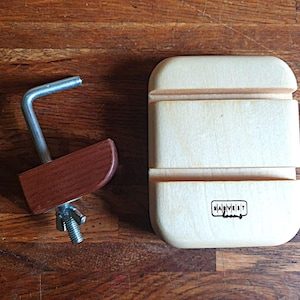May include: A wooden phone stand with a light finish, featuring a rectangular base with a slot and the text "HARVEST looms". A separate piece includes a dark brown wooden piece with a metal arm and a wing nut.