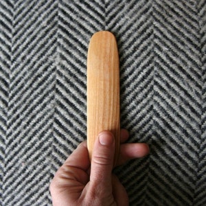 Peut inclure: Gros plan d'un outil en bois avec une extrémité arrondie, tenu dans une main sur un fond à motif en chevrons noir et blanc.