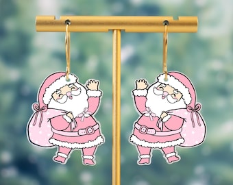 May include: A pair of pink Santa Claus earrings. Each earring depicts a cartoon Santa with a white beard, pink suit, and a sack of gifts. The earrings hang from gold-coloured hoops.