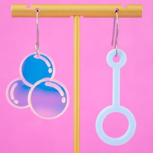 May include: A pair of iridescent blue earrings. One earring is shaped like three bubbles, the other is shaped like a bubble wand.