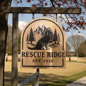 May include: Wooden sign for "Rescue Ridge" with a dog silhouette, mountains, and trees. The sign is hanging outdoors and includes the text "EST. 2026". The sign is made of light-colored wood and is hanging from a wooden beam.