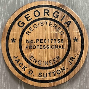 May include: A round wooden sign with black lettering that reads "Georgia Registered Professional Engineer No. PE017755 Jack D. Sutton, Jr."