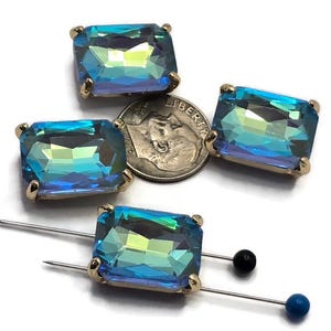 May include: Four rectangular, iridescent blue-green rhinestones with gold-colored prongs. A US dime is next to the rhinestones for size comparison. Two pins with black and blue heads are also in the image.