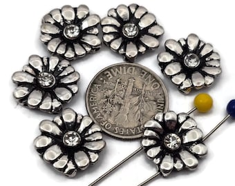 May include: Close-up of silver-toned flower-shaped embellishments with a clear crystal center. A US dime is next to the embellishments for size comparison. Two pins with yellow and blue heads are also visible.