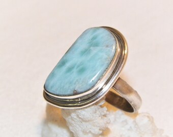 Op de afbeelding: Een zilveren ring met een lichtblauwe edelsteen. De edelsteen heeft een uniek patroon van witte en blauwe swirls.