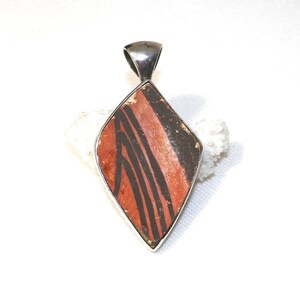 May include: A silver pendant featuring a diamond-shaped piece of red and black pottery with a geometric pattern.